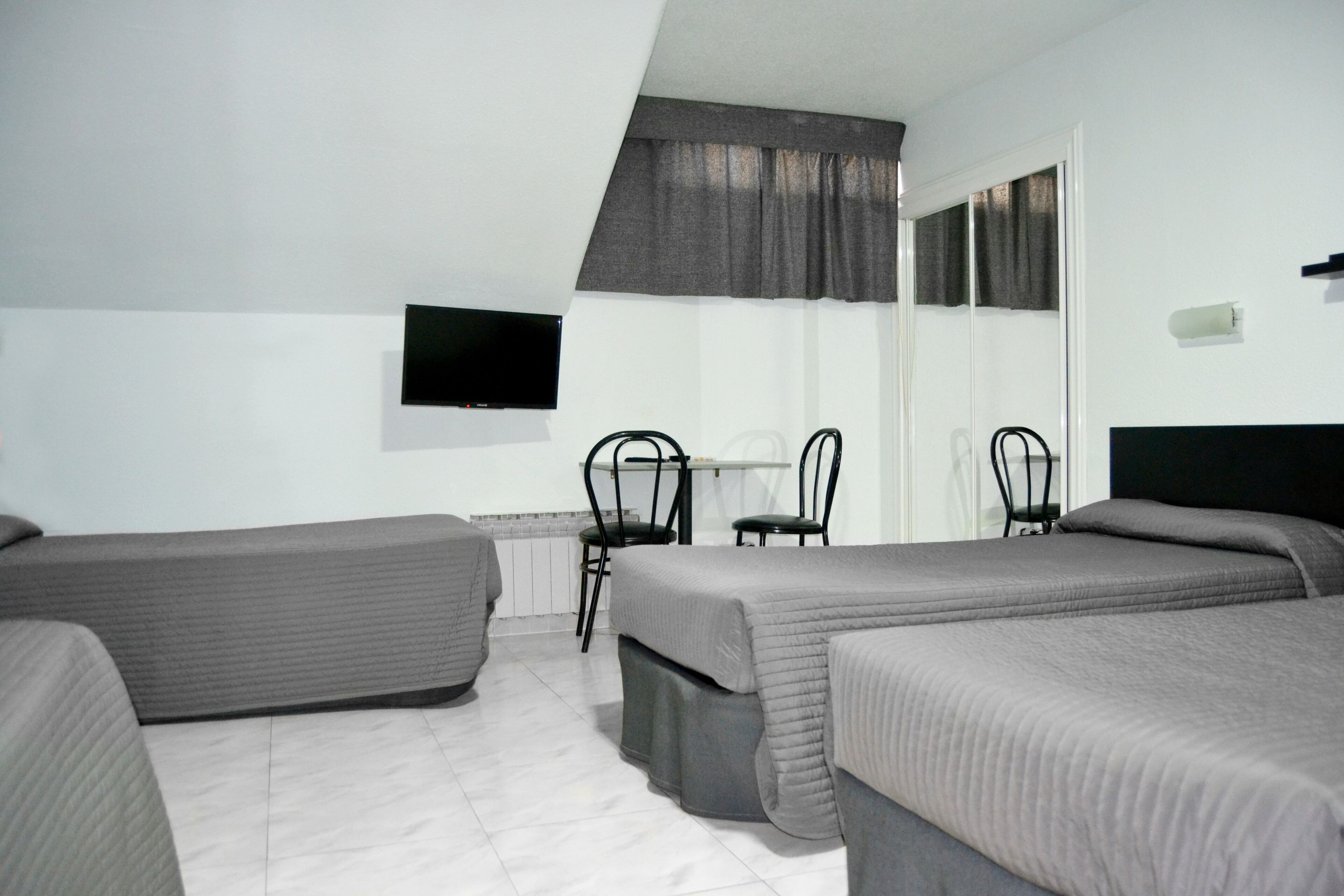 Een hotelkamer met twee eenpersoonsbedden, een bureau met stoel, een aan de muur bevestigde televisie en een raam met gordijnen.
