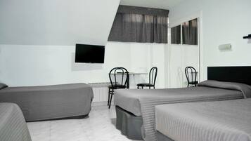 Een hotelkamer met twee eenpersoonsbedden, een bureau met stoel, een aan de muur bevestigde televisie en een raam met gordijnen.