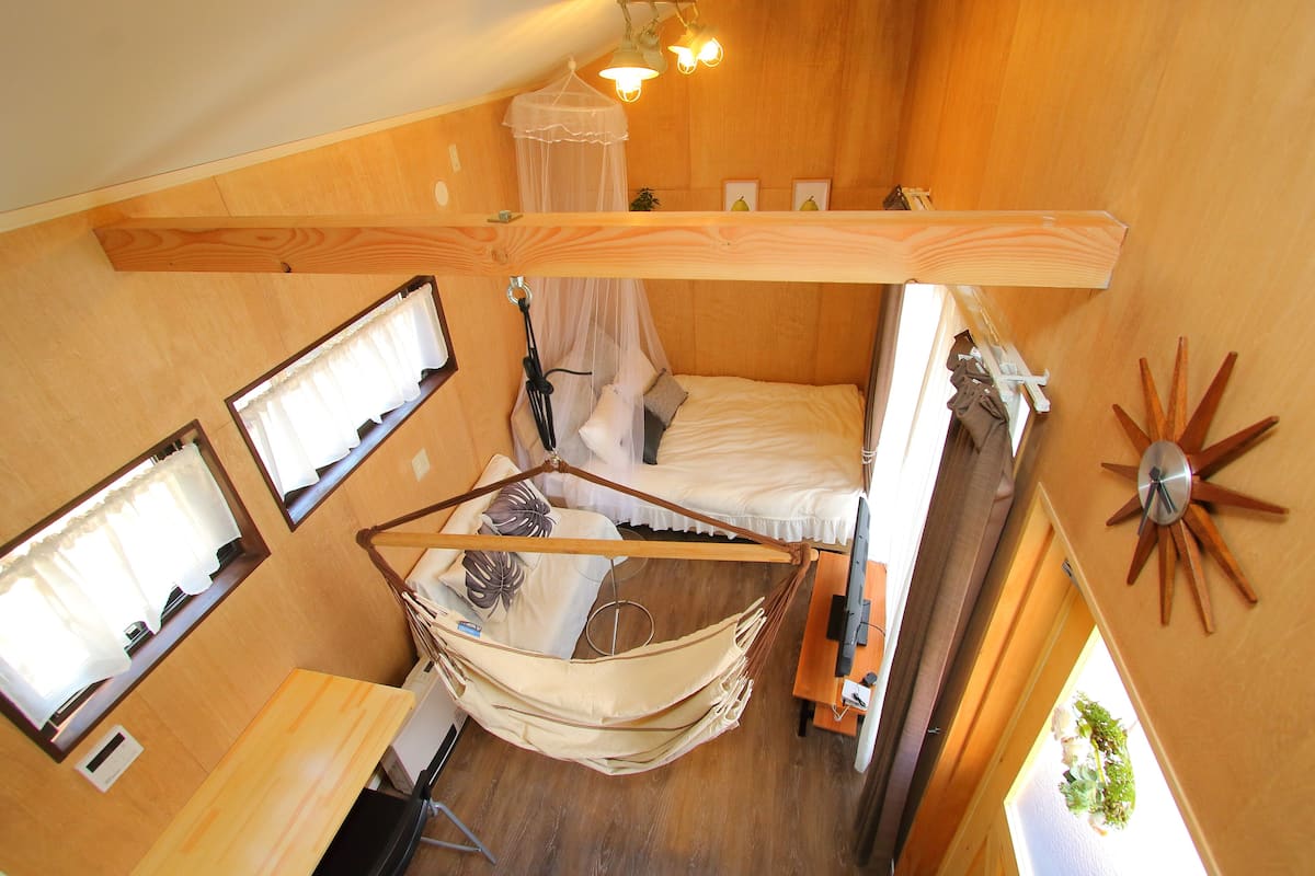 A compact room with a bunk bed, a hanging hammock, a small table, and a bedside lamp.