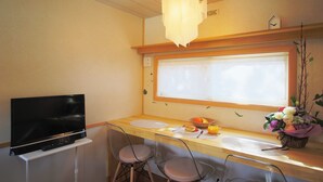 Cocina compacta con una televisión de pantalla plana, dos taburetes de bar, una ventana con persianas y un pequeño arreglo floral en la encimera.