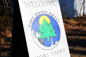 Señal de bienvenida del Tiny House Hotel Moritabby, con el logotipo de un gato y árboles.