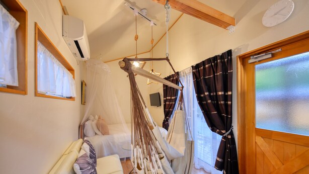 Una habitación con cama, una silla colgante, una ventana con cortinas y una puerta de madera.