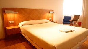 Une chambre d’hôtel avec un grand lit, une table de chevet, un bureau avec un ordinateur portable et une chaise.
