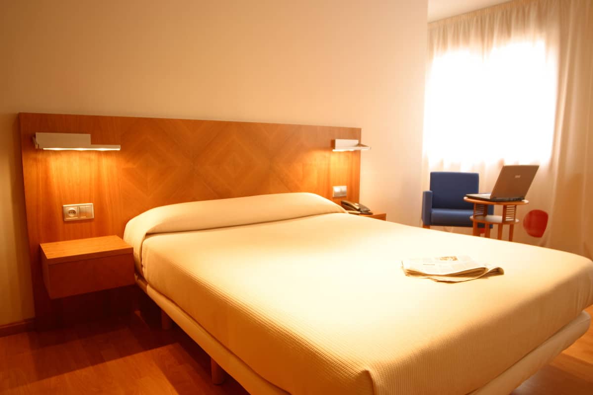 Une chambre d’hôtel avec un grand lit, une table de chevet, un bureau avec un ordinateur portable et une chaise.