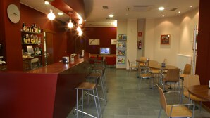 Un espace bar avec des tabourets, un comptoir et des étagères remplies de bouteilles. La salle à manger est aménagée avec des tables et des chaises.