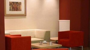 Un hall d’hôtel moderne avec un canapé beige, des fauteuils rouges et une petite table sur laquelle se trouvent une théière et une tasse.