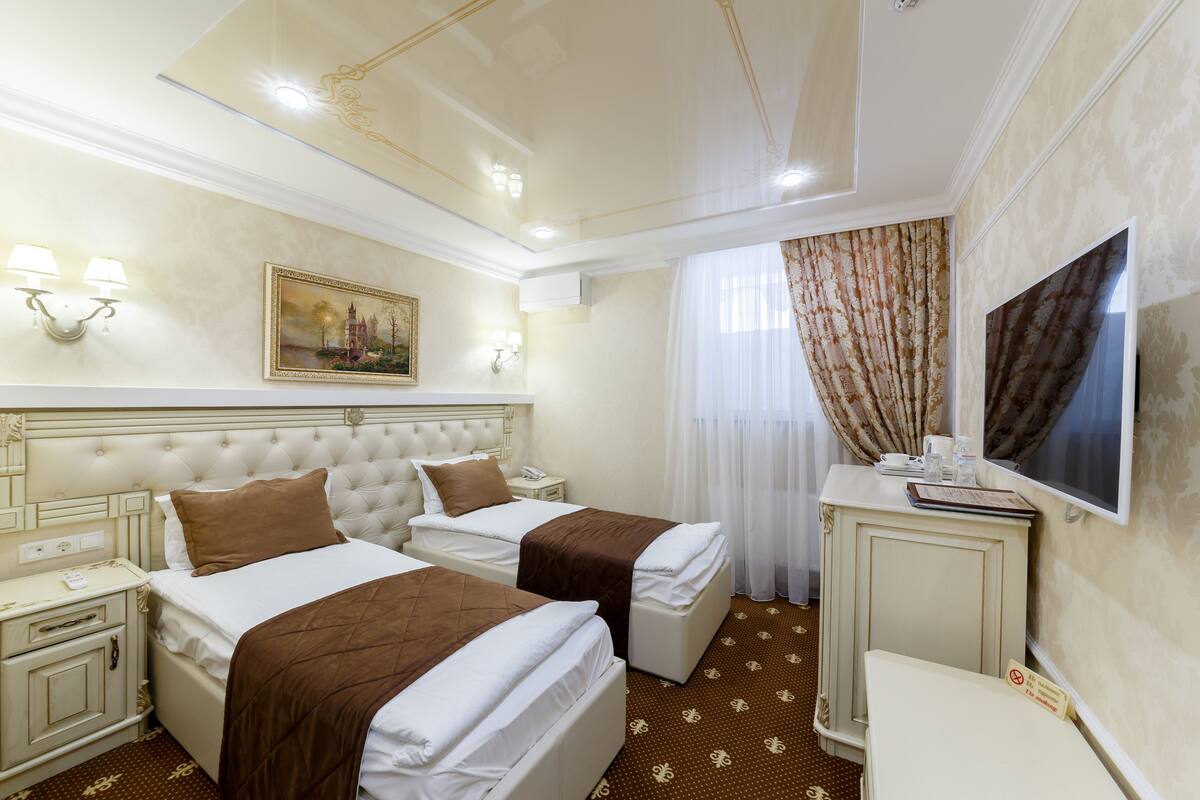 A hotel room with two beds, a television, a desk, and a painting on the wall.