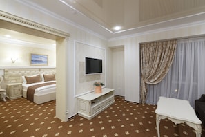 A hotel room with a bed, a TV mounted on the wall, a small table, and a window with curtains. - Chevalier Hotel & Spa (Bukovel)