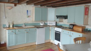 A kitchen with teal cabinets, a white dishwasher, a microwave, a stove, and a wooden countertop.