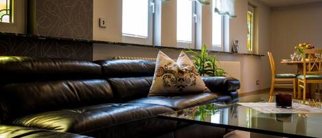 A living room with a leather sofa, a glass coffee table, and a dining area with a wooden table and chairs.