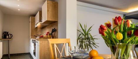 A modern kitchen with wooden cabinets, a dining table with a vase of tulips, oranges, and a glass pitcher.