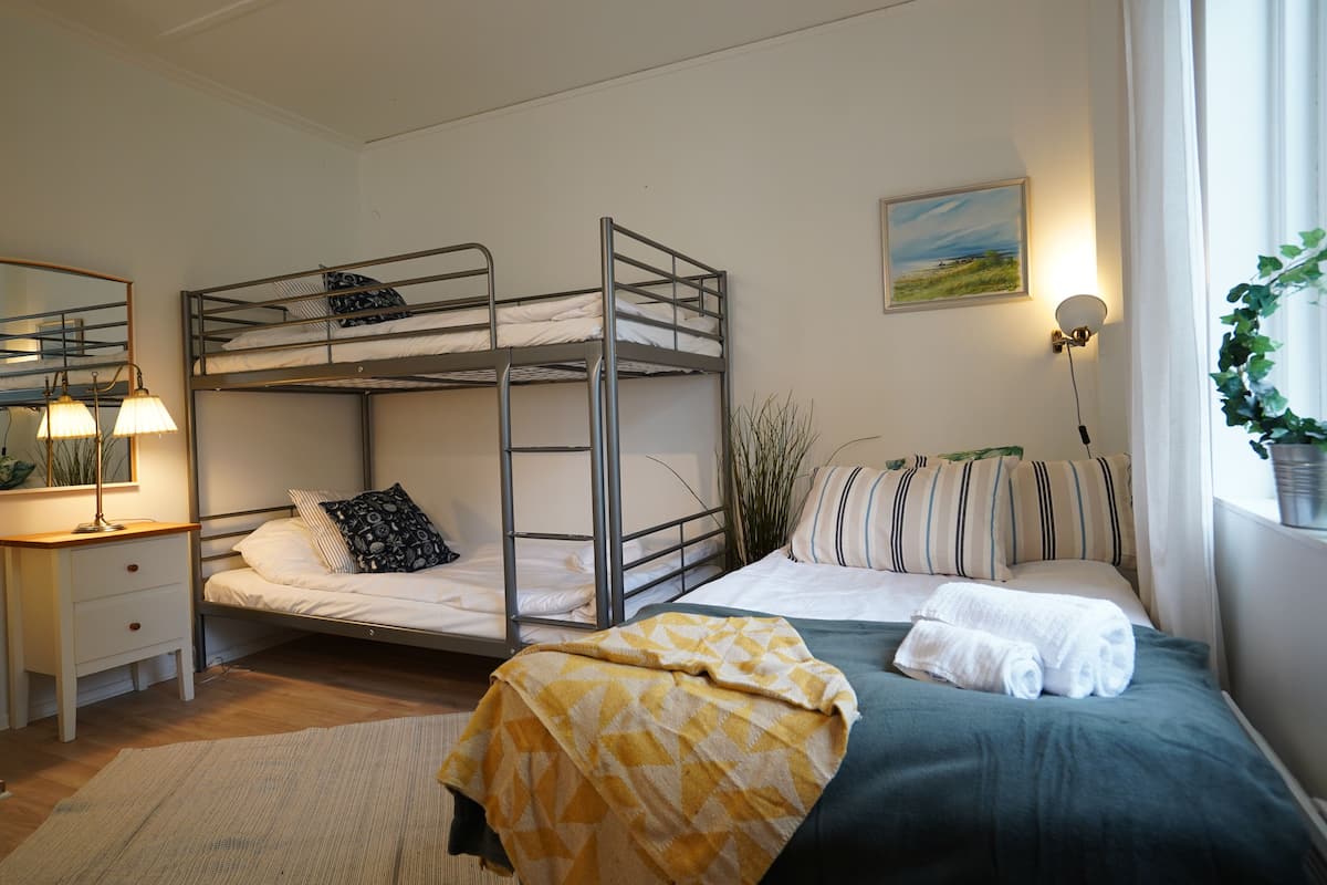 Een slaapkamer met een stapelbed, een bureau, een lamp en een raam met een plant.