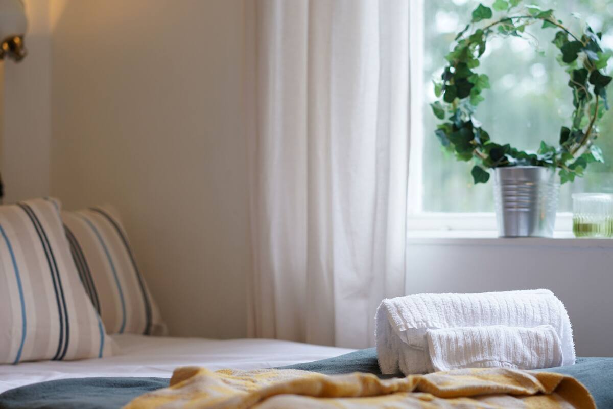 Een bed met een gele deken, een kamerplant en een raam met gordijnen.