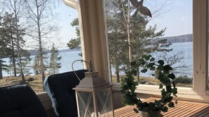 Een houten tafel met een glazen lantaarn, een potplant en uitzicht op een meer en bomen door een raam.