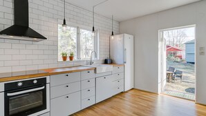 Een moderne keuken met witte kasten, een houten aanrecht, een zwarte afzuigkap en een raam met potplanten.