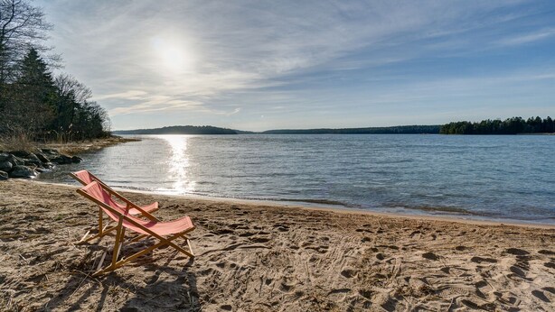 Een strand met een rij lege strandstoelen gericht op het water.