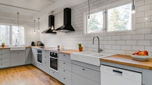 Een moderne keuken met witte kastjes, een houten aanrecht, een inbouwoven, een vaatwasser en een raam dat voor daglicht zorgt.