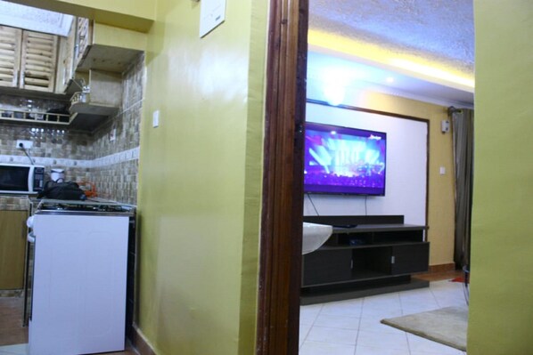 Una cocina compacta con microondas, estufa y un televisor de pantalla plana montado en un mueble oscuro.
