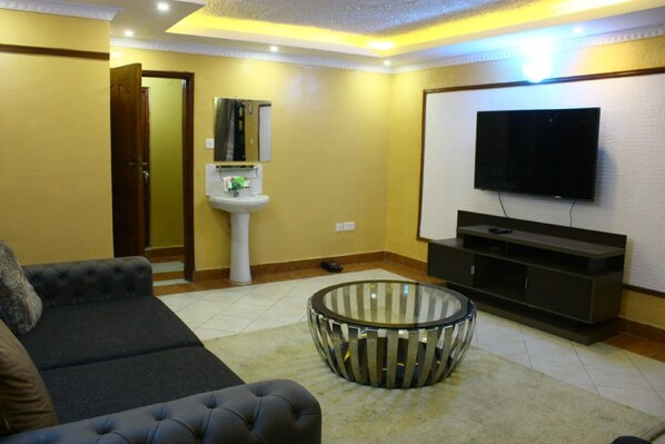 A living room with a sofa, a glass coffee table, a television, and a sink.