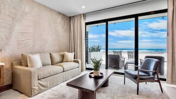 Ein modernes Wohnzimmer mit einer Couch, Sesseln, einem Couchtisch und Blick auf den Strand.