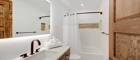 A modern bathroom with a wooden vanity, a large mirror, a bathtub, and a toilet.