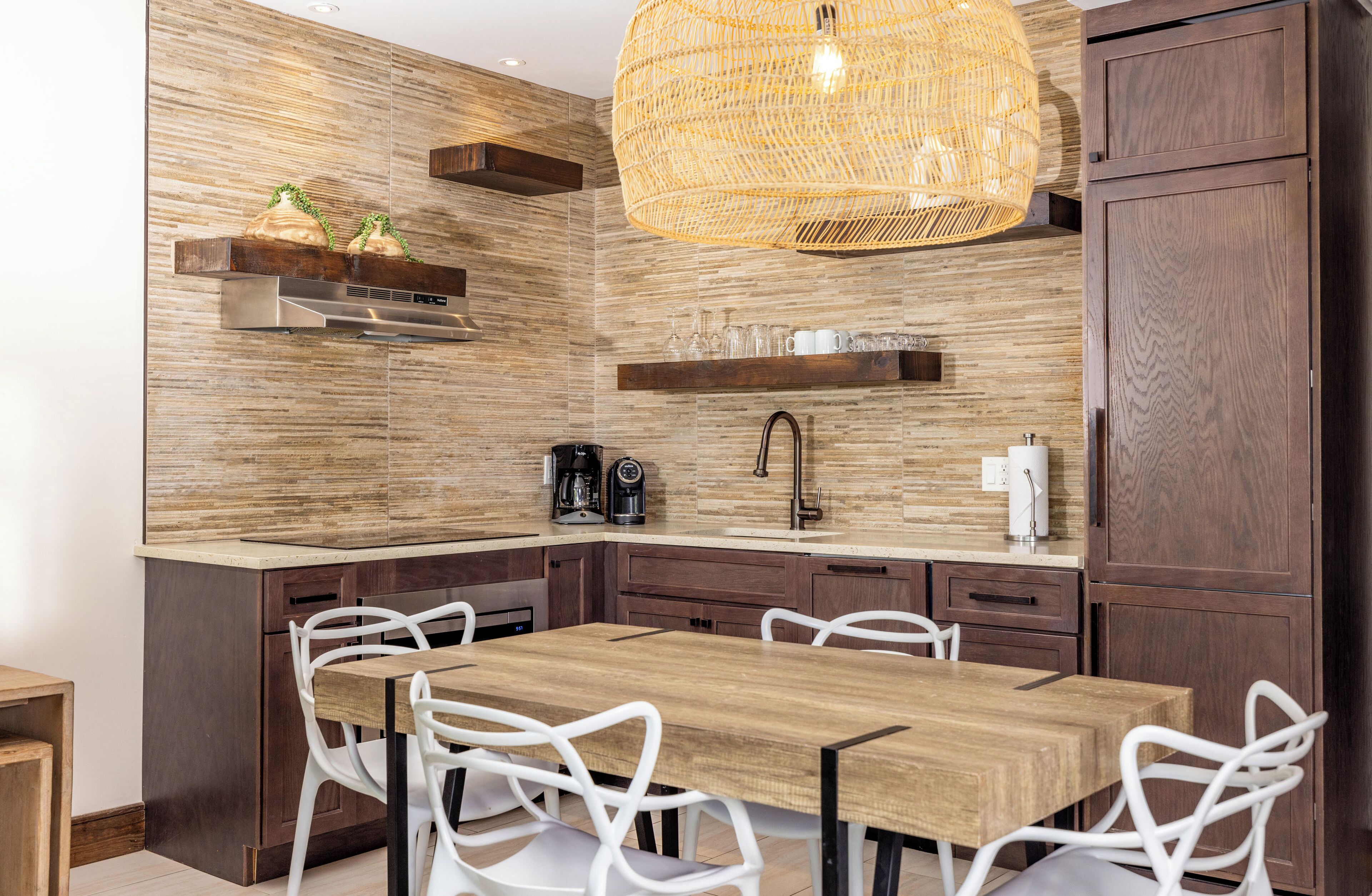 Une cuisine moderne avec un plan de travail en bois, des chaises blanches et un luminaire suspendu.
