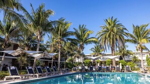 A pool area with lounge chairs and umbrellas, surrounded by palm trees. - Bali Hai Beachfront Resort and Spa (Holmes Beach)