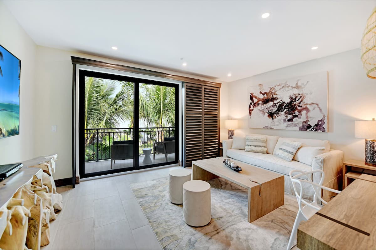 A modern living room with a large sliding glass door leading to a balcony with palm trees.