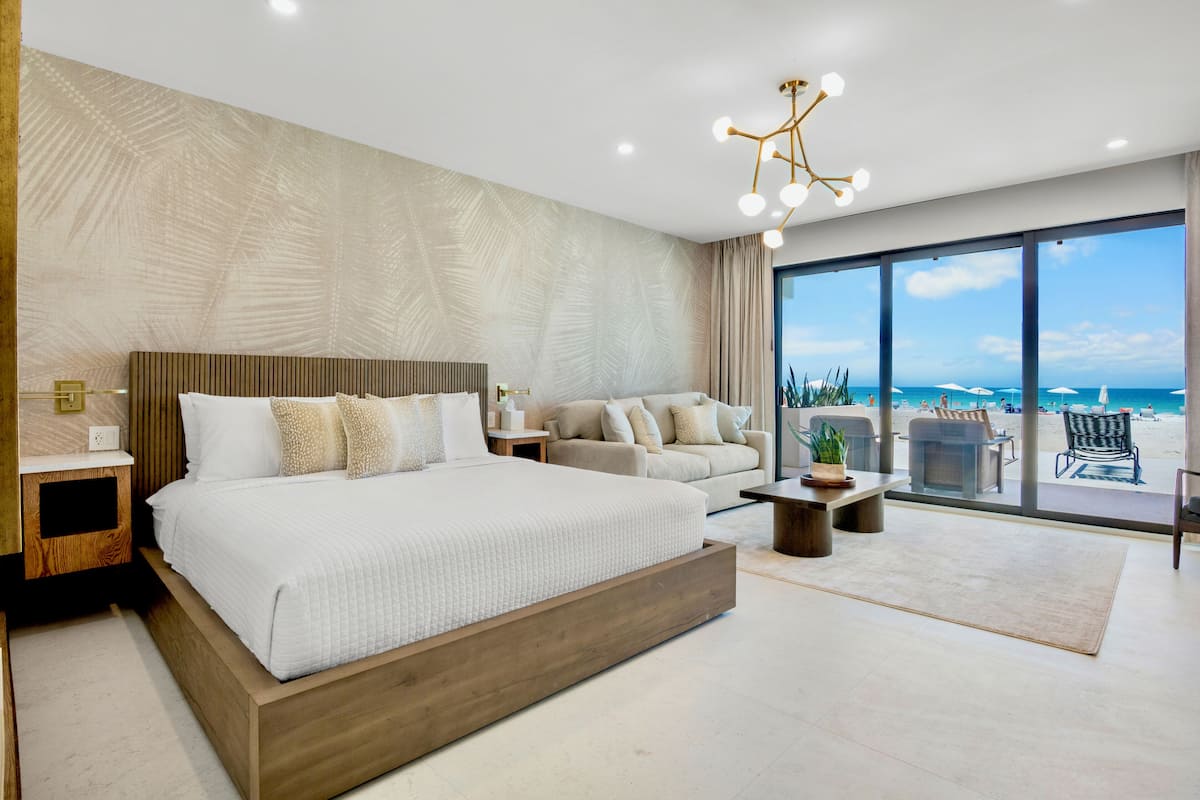 A modern bedroom with a large bed, a sofa, a coffee table, and a view of the beach.