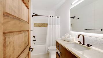 A modern bathroom with a wooden vanity, a white bathtub, and a large mirror.