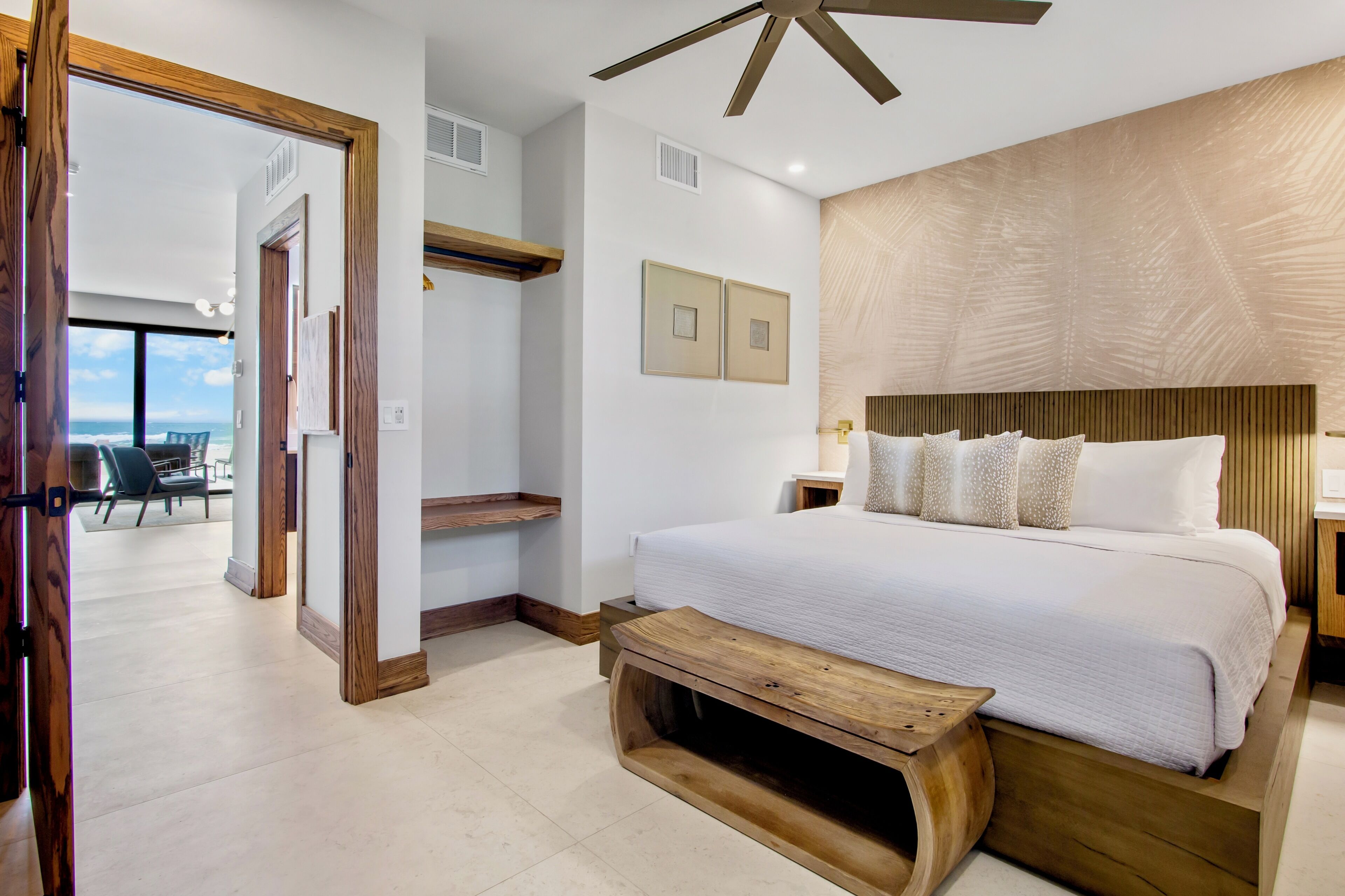 A bedroom with a large bed, wooden headboard, and a view of the ocean through an open door.