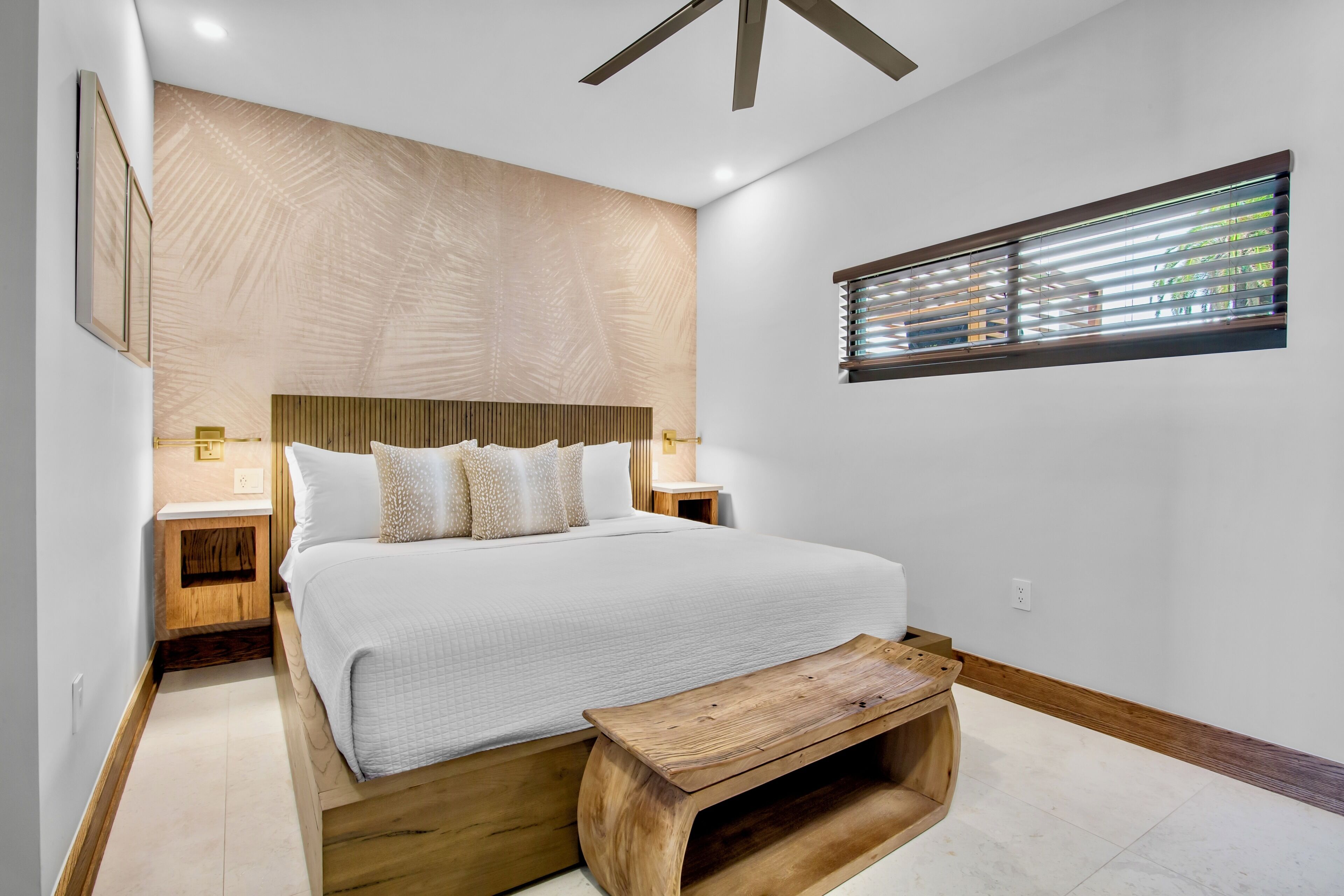 A modern bedroom with a large bed, wooden headboard, bedside tables, and a built-in bench.