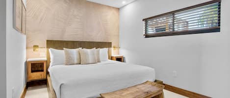 A modern bedroom with a large bed, wooden headboard, bedside tables, and a built-in bench.