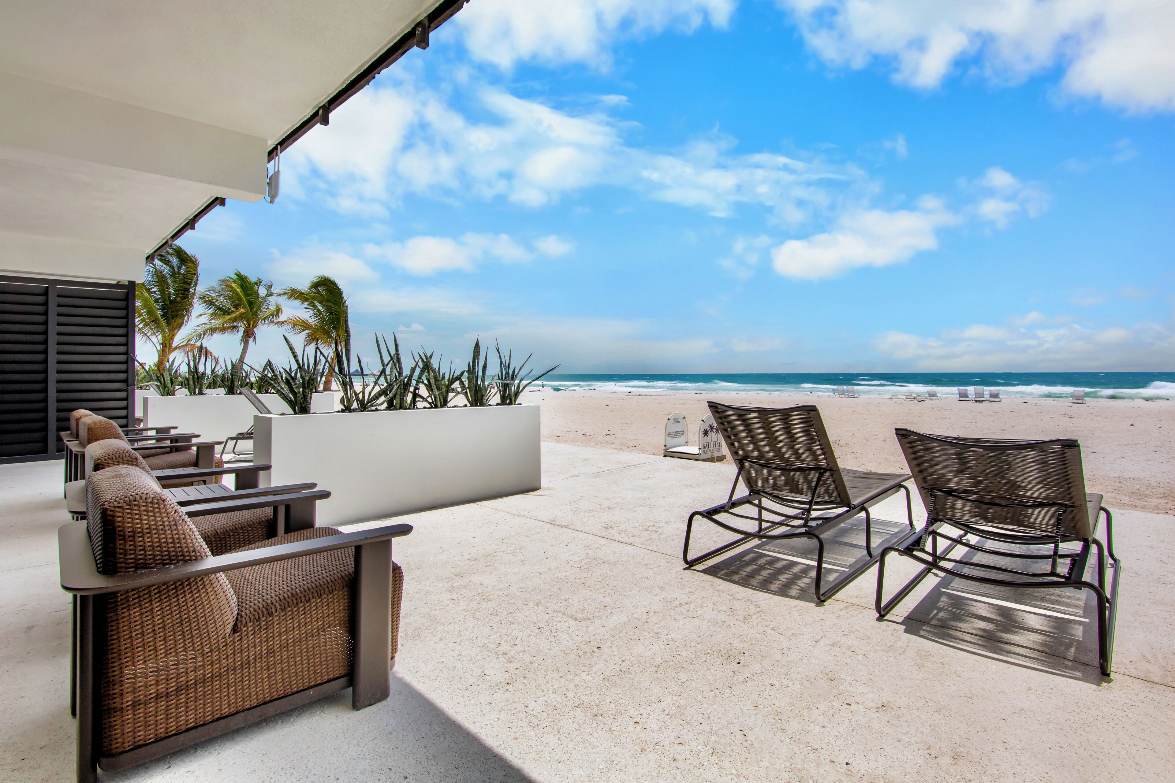 A beachside patio with wicker furniture, a view of the ocean, and a palm tree.