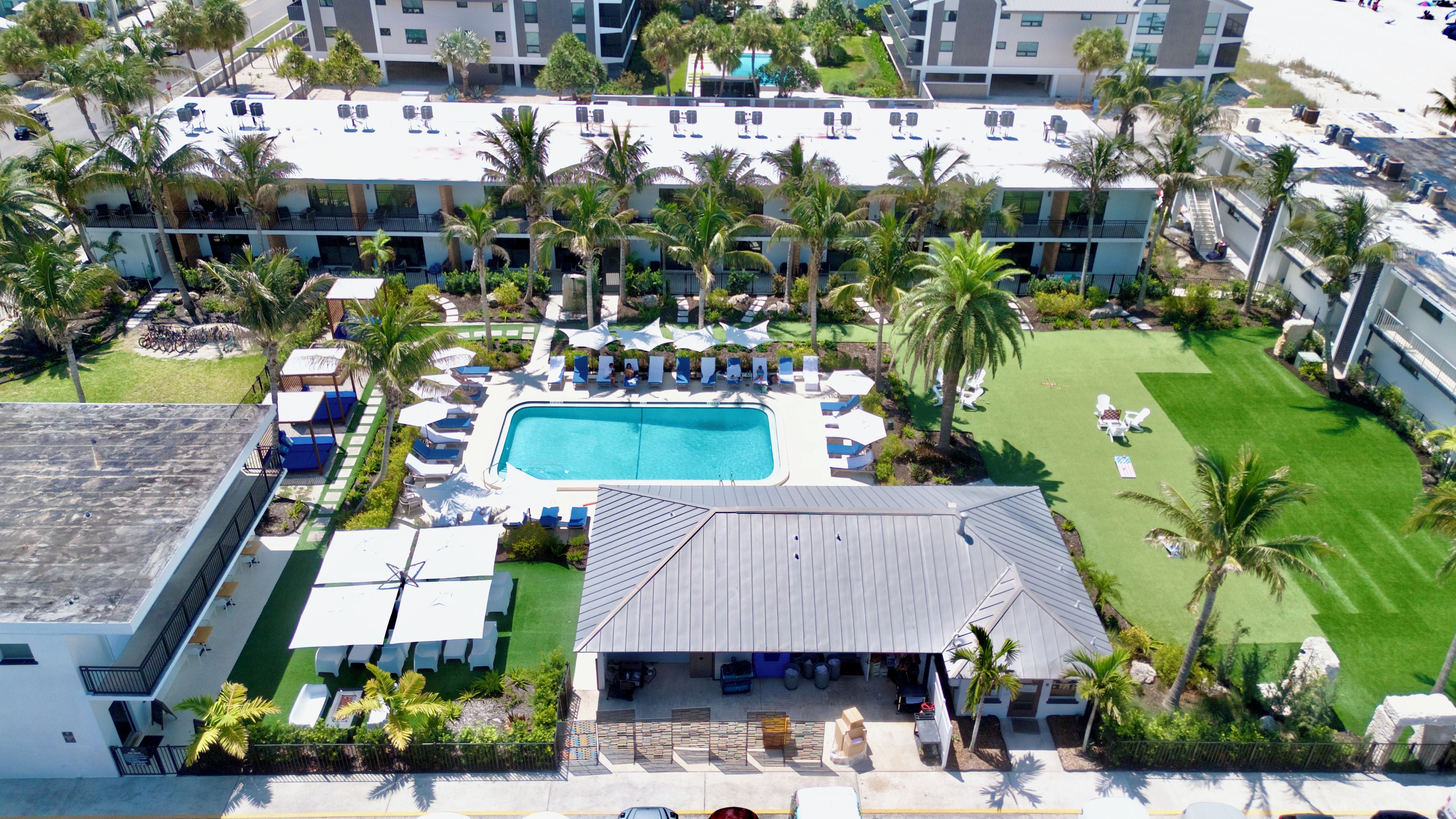 Oversigtsbillede af et resort med swimmingpool, liggestole og palmer.