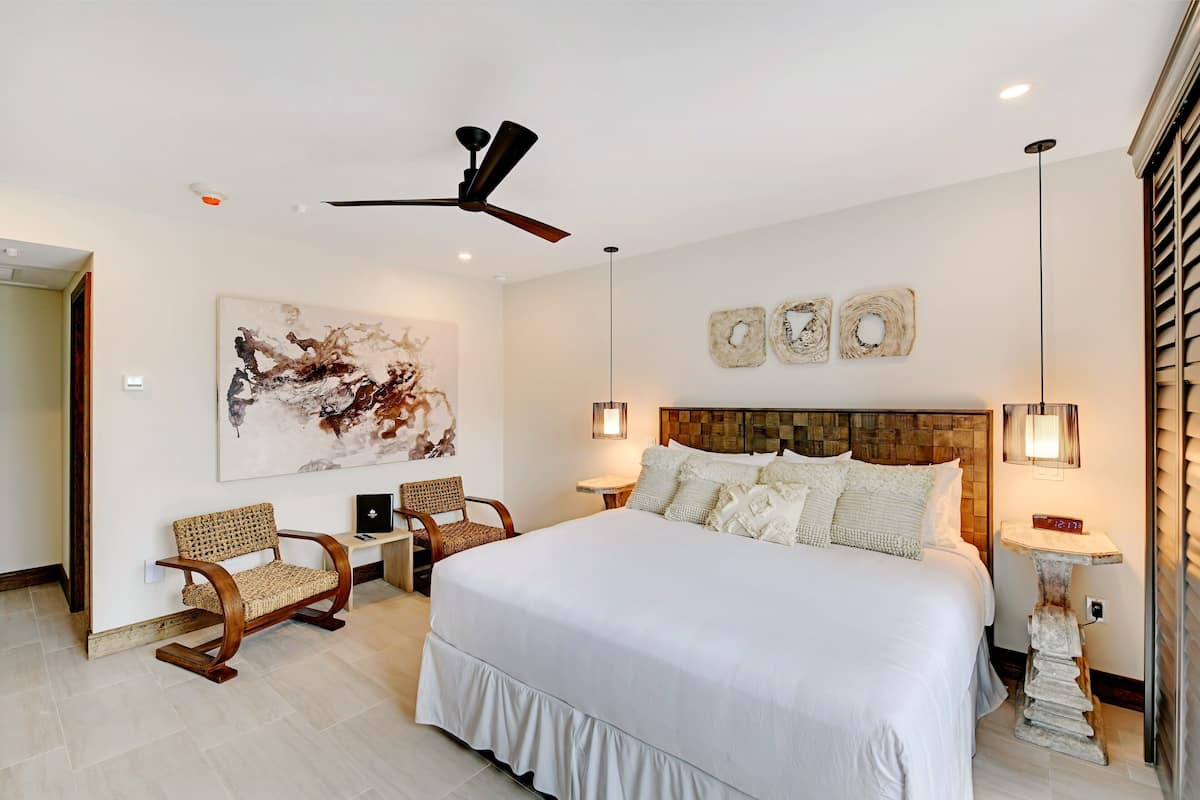 A spacious bedroom with a large bed, a ceiling fan, and a modern art piece on the wall.