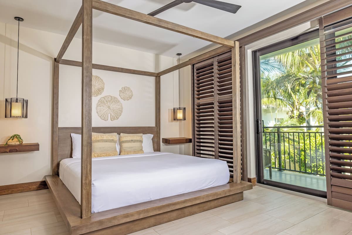 A four-poster bed with a wooden frame, a balcony with a view of palm trees, and wall decor with circular patterns.