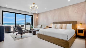 Un dormitorio moderno con una cama grande, un área de descanso con una mesita de centro y vistas al océano.