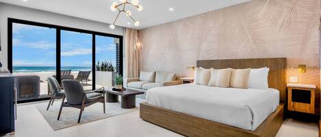 Un dormitorio moderno con una cama grande, un área de descanso con una mesita de centro y vistas al océano.