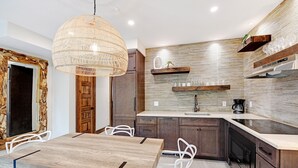 A modern kitchen with a wooden dining table, white chairs, and a hanging light fixture. - Bali Hai Beachfront Resort and Spa (Holmes Beach)