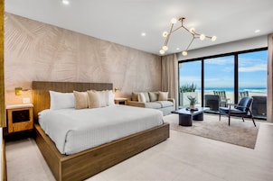 A modern bedroom with a large bed, a sofa, a coffee table, and a view of the ocean.