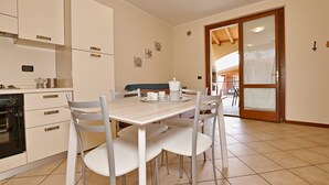 A modern kitchen with white cabinets, a dining table with chairs, and a view of the dining area through a glass door. - Appartamento Romantica (Manerba del Garda)