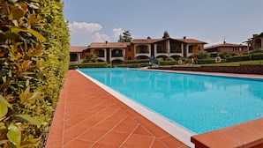 A swimming pool with a tiled deck, surrounded by neatly trimmed hedges and a row of buildings with a consistent architectural style. - Appartamento Romantica (Manerba del Garda)