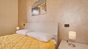 A neatly made bed with a yellow quilt, a white pillow, and a bedside lamp on a white nightstand. - Appartamento Romantica (Manerba del Garda)