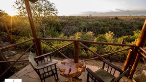 Una terraza de madera con dos sillas y una mesa peculiar, con vistas a un paisaje natural.