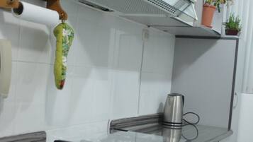 A kitchen with white cabinets, a stainless steel range hood, a microwave, and a small potted plant.