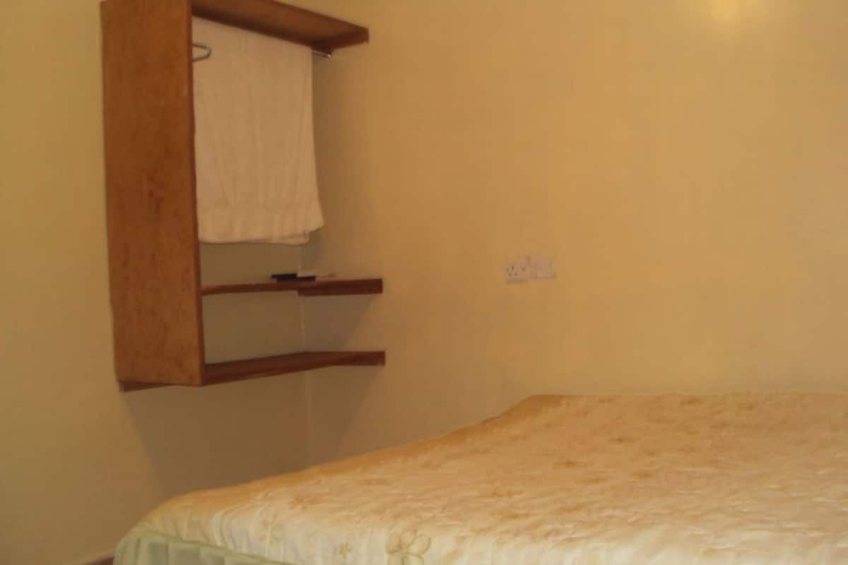 A bedroom with a bed, a wooden shelf, and a towel hanging on the wall.