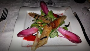 A square white plate with a salad consisting of greens, radicchio, and a piece of bread.