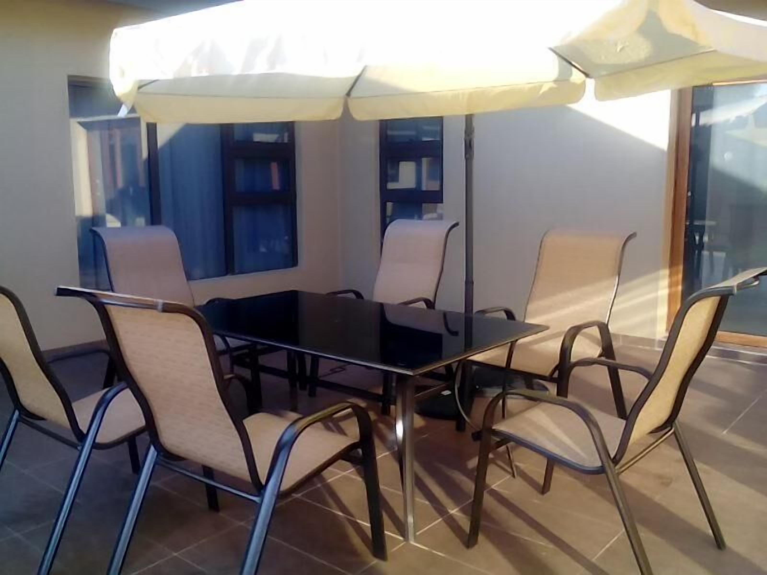 Un comedor con una mesa de vidrio y sillas, rodeado por una sombrilla blanca.