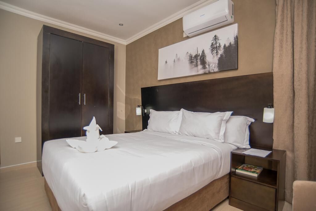 Una habitación de hotel con una cama grande, un armario, una mesita de noche y un cuadro en la pared.